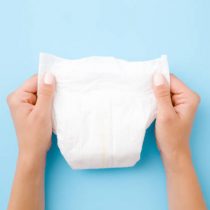 Woman hands holding white baby diaper on pastel blue background. Closeup. Top view.